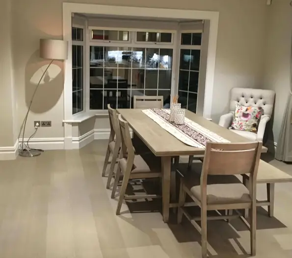 Suburban home dining room project featuring light gray hardwood floors and a wooden dining table set by a bay window