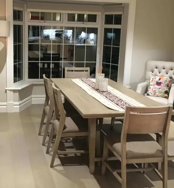 Suburban home dining room project featuring light gray hardwood floors and a wooden dining table set by a bay window